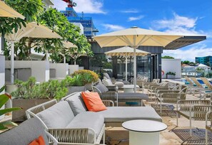 Ein Außenbereich mit Lounge-Möbeln aus Rattan, Sonnenschirmen und Topfpflanzen.