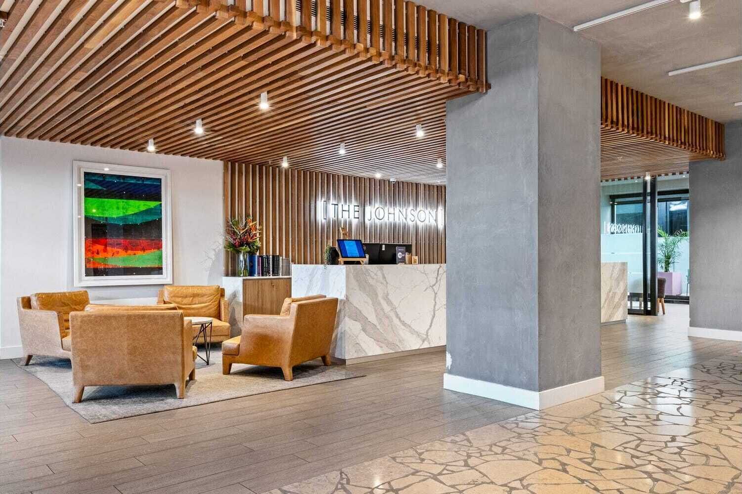 A modern reception area with a wooden slatted ceiling, a marble reception desk, and a seating area with leather chairs.