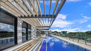 Een modern dakzwembad met een glazen balustrade, grote ramen en uitzicht op een heldere lucht.
