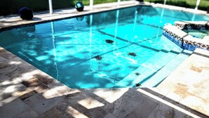 Una piscina con agua azul cristalina, bordes azulejados y una terraza de piedra alrededor.