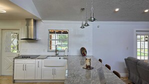 Una cocina moderna con armarios blancos, encimera de mármol e iluminación colgante.