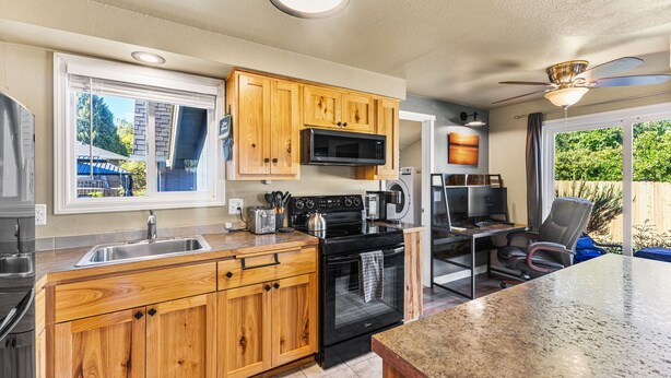 A modern kitchen with wooden cabinets, a built-in microwave, a stove, and a large island with a granite countertop. - Remodeled Albany 1BDRM, modern, pet friendly fenced yard, work station, laundry! (Albany)