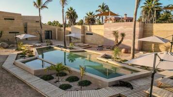 Un área de piscina con muelle de madera, palmeras y sillones de descanso.