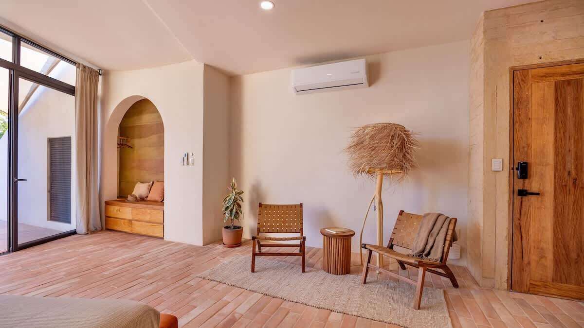 Una habitación amplia con un gran ventanal, un banco de madera, una planta en maceta y una puerta rústica.