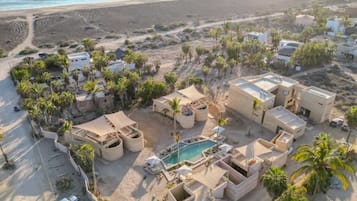 Vista aérea de un complejo turístico con varias edificaciones, una piscina y palmeras.