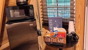 A kitchenette with a coffee maker, microwave, and refrigerator. There's a sign for a coffee bar and a window with blinds.