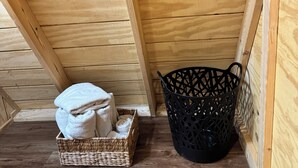 Eine Ecke einer Holzhütte mit einem gewebten Korb und einem schwarzen Plastikkorb auf dem Boden.