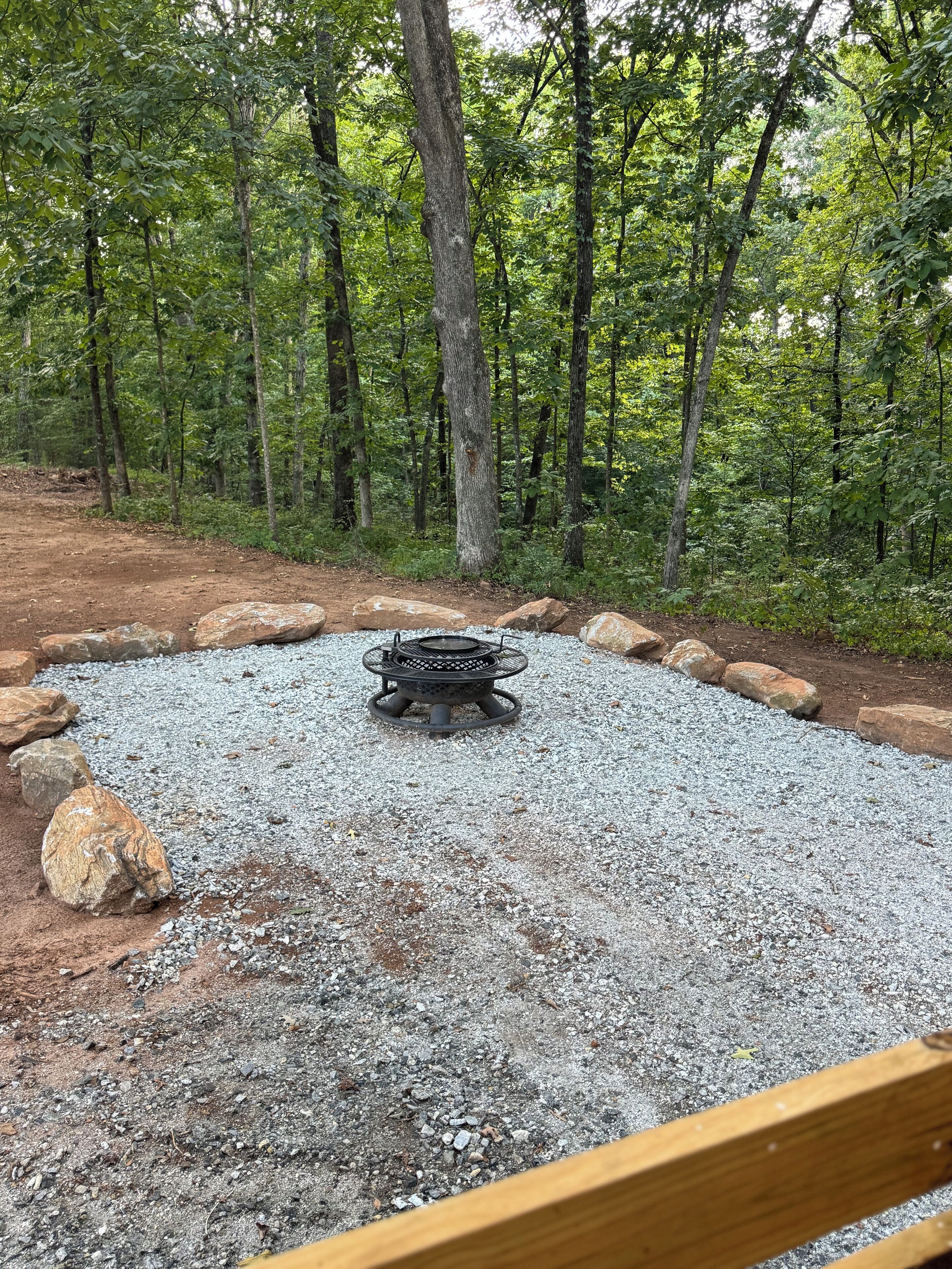 A gravel fire pit surrounded by rocks in a forested area.