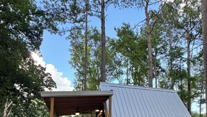 A small, rustic cabin with a sloped metal roof and wooden deck, surrounded by trees.