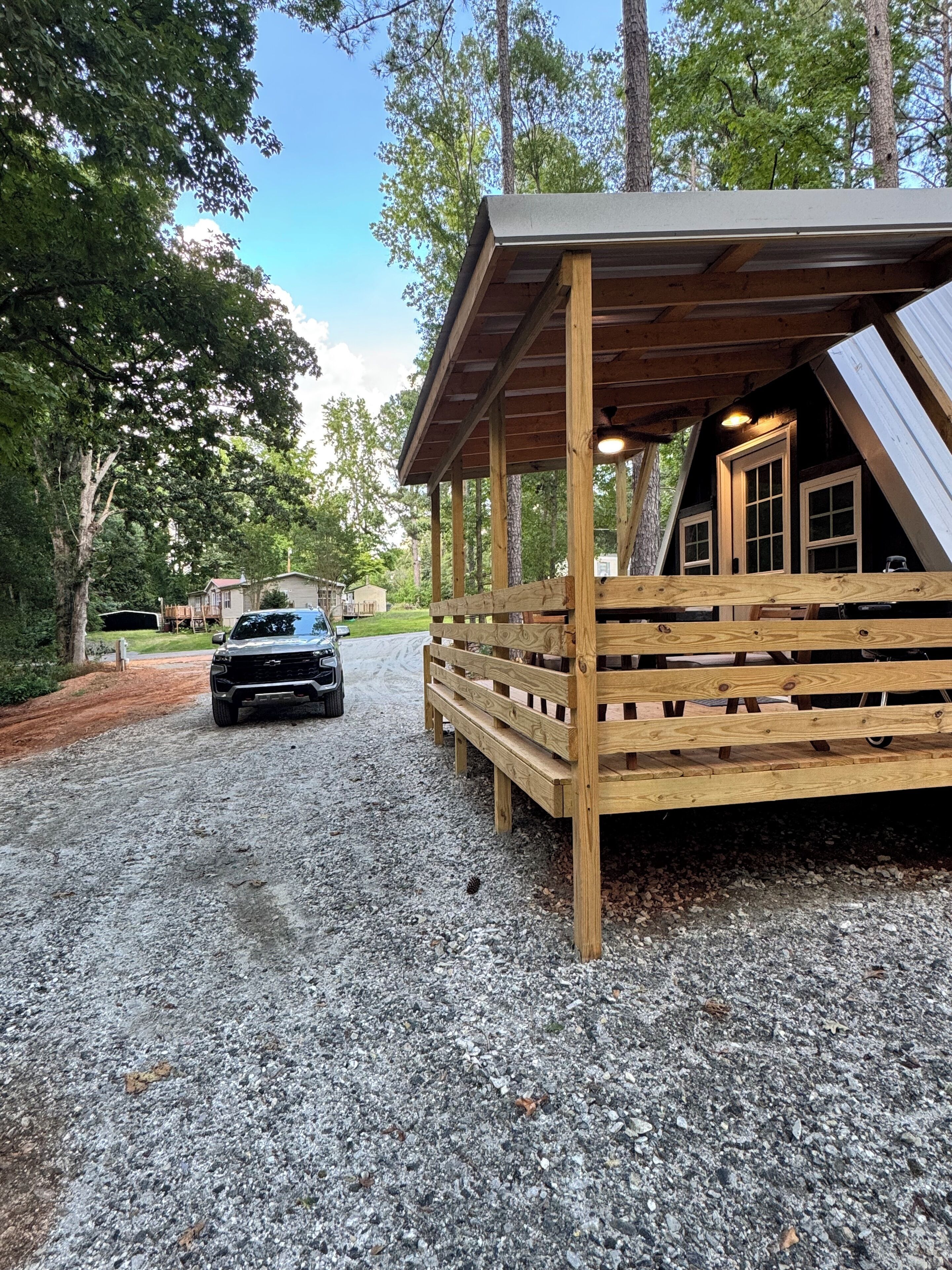 A rustic cabin with a gravel driveway and a black vehicle parked in front.