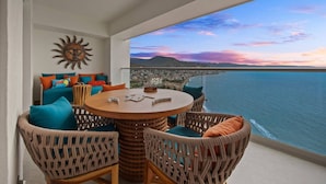 A balcony with wicker furniture, a round table, and a view of the ocean and cityscape during sunset. - Harbor NT2507 by Moikkarentals (Puerto Vallarta)