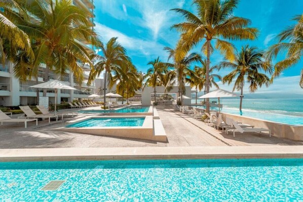 A pool area with lounge chairs and palm trees, overlooking the ocean.