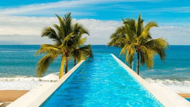 A swimming pool with a view of the ocean and palm trees. - Harbor NT2507 by Moikkarentals (Puerto Vallarta)