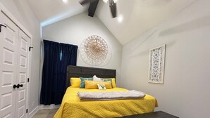 A bedroom with a bed, a bench, a door, a wall with a circular artwork, and a framed picture.