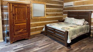 A wooden cabin bedroom with a bed, a window, a door, and an air conditioning unit. - “The Bear Cave” WhittleSticks Cabin in Lancing TN (Lancing)