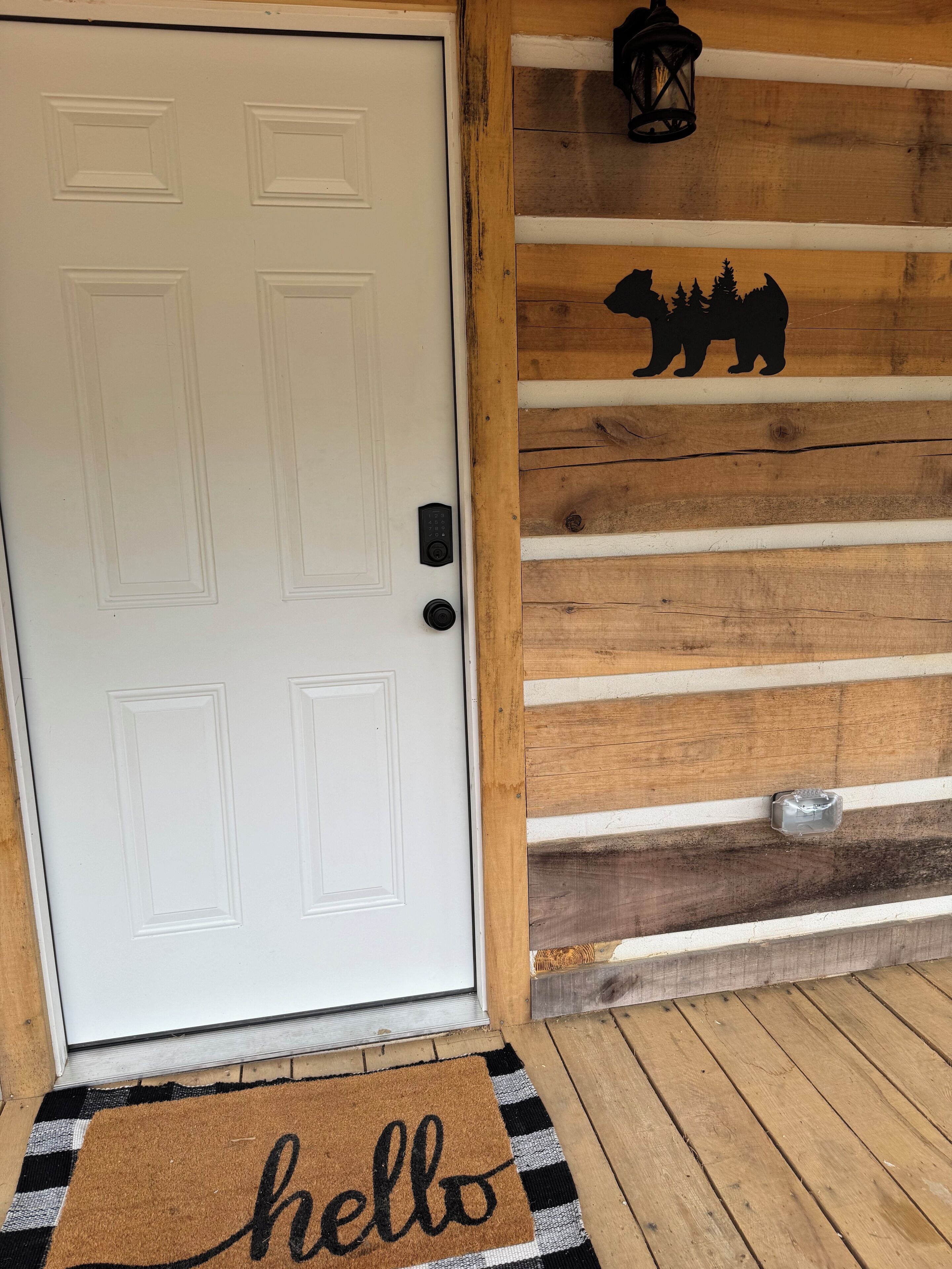 A white door with a keypad lock, a wooden wall with a bear silhouette, and a 'hello' doormat.