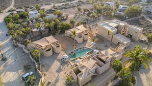 An aerial view of a resort with multiple buildings, a swimming pool, and palm trees.