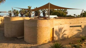 A desert-style building with a flat roof, large windows, and a shaded outdoor area with a canopy.