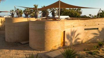 Un edificio de estilo desértico con tejado plano, ventanas amplias y un área exterior sombreada con toldo.