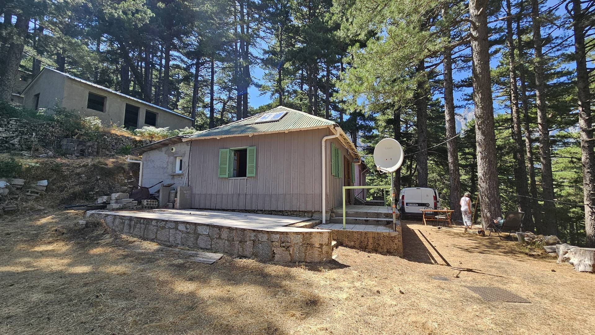 Une petite cabane en bois, surmontée d’un toit en métal, entourée d’arbres.