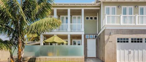A two-story residential building with a covered patio, a garage, and a palm tree.