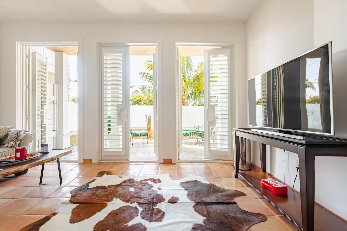 A living room with a television, a cowhide rug, and a view of a patio with outdoor furniture.