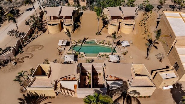 Luchtbeeld van een resort met meerdere gebouwen, een centraal gelegen zwembad en palmbomen.