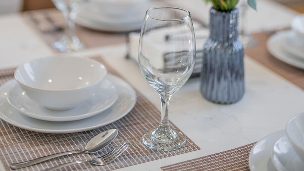 A dining table set with white plates, bowls, and cutlery, a vase with pink flowers, and a glass. - 2BD/2BA Apartment near DT Alhambra (Alhambra)