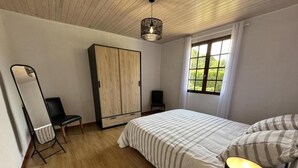 A bedroom with a bed, a wardrobe, a chair, a mirror, and a window with a view of greenery. - Gîte Jean de Nasse - CASTETS (CASTETS)