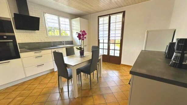 A kitchen with white cabinets, a black countertop, and a dining table with chairs. - Gîte Jean de Nasse - CASTETS (CASTETS)