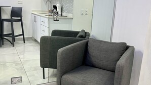 Una cocina moderna con armarios blancos, un sofá gris y un comedor con una silla negra.