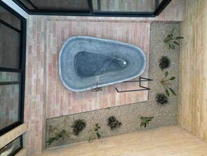Ein Wellnessbereich mit einer Steinbadewanne, einer Holzbank und kleinen Pflanzen.