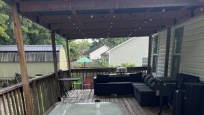 A wooden deck with a glass table, outdoor furniture, and a pergola.