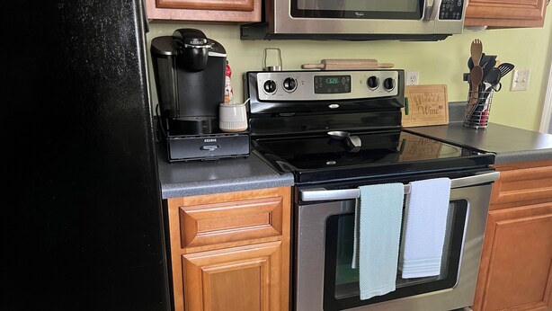 A kitchen with a Keurig coffee maker, a microwave, a stove, and wooden cabinets.