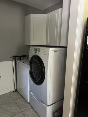 A compact laundry room with a front-loading washer and dryer, white cabinetry above, and a tiled floor.