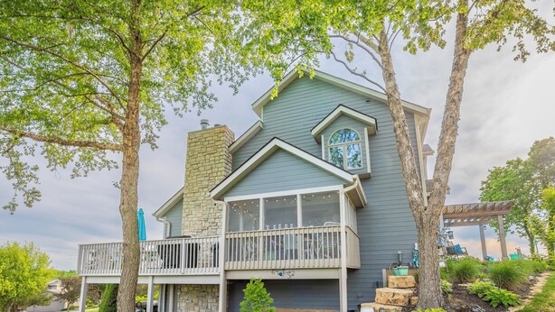 A two-story house with a balcony, a chimney, and a garden with various plants and a small tree. - Spacious 3BR*Ensuites | Hot Tub*Fire Pit*Game Room*Coffee Bar*Stunning Sunsets! (Galena)