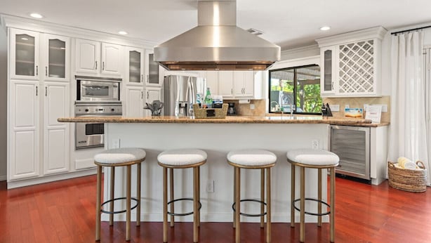 A modern kitchen with white cabinetry, stainless steel appliances, and a central island with stools. - Coachella Casa Spanish-Style Oasis with Pool in Indio (Indio)