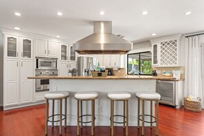 A modern kitchen with white cabinetry, stainless steel appliances, and a central island with stools. - Coachella Casa | Heated Pool & Spa (Indio)