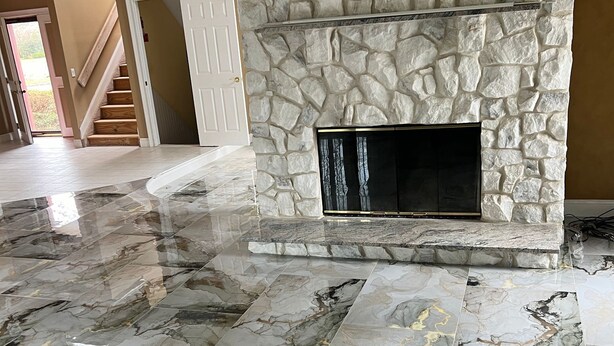 A spacious living area with a stone fireplace, marble flooring, and a staircase leading to another room.