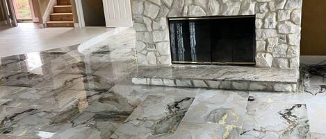 A spacious living area with a stone fireplace, marble flooring, and a staircase leading to another room.