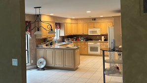 A modern kitchen with a central island, wooden cabinets, a microwave, and a glass shelf unit.