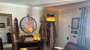 Una sala de estar con un sofá de cuero negro, una mesa de centro de madera, un gran reloj de pared, una chimenea y un espejo.
