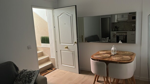 A modern kitchen with stainless steel appliances, a dining area with a wooden table and woven placemats, and a staircase leading to an outdoor area.
