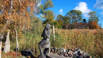 Eine Skulptur zeigt eine Figur in einer natürlichen Umgebung mit Bäumen und blauem Himmel.