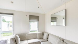 A modern, well-lit room with a sectional sofa, large windows, and a wall-mounted mirror. - Mobile Home in Veuzain-sur-loire With Garden (Veuzain-sur-Loire)