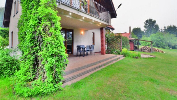 Une maison à deux étages dotée d’un patio couvert, d’une terrasse en bois et d’un jardin.