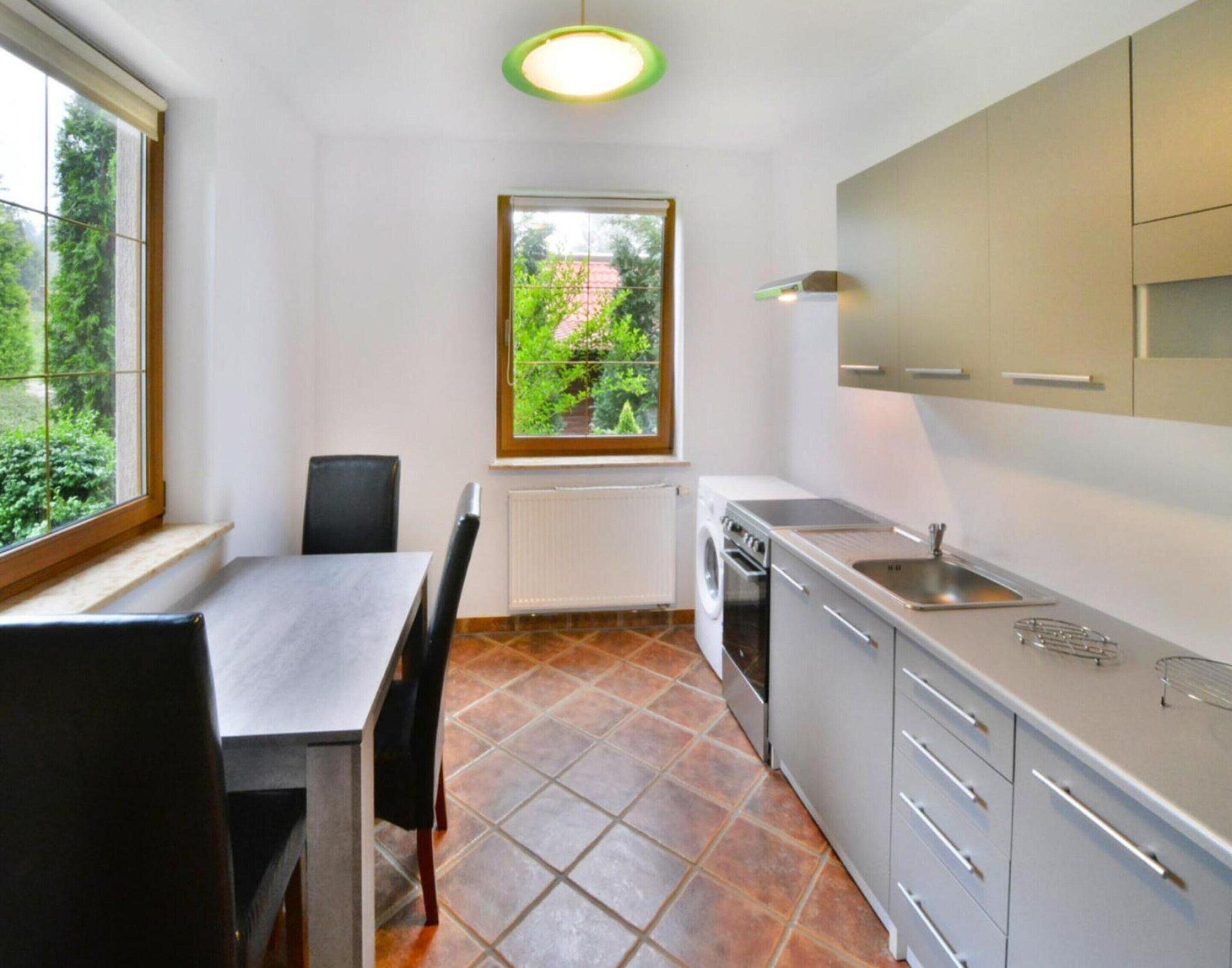 A compact kitchen with a dining table, chairs, a window with a view of greenery, and modern appliances.