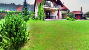 Une maison à deux étages dotée d’un balcon, entourée d’une pelouse bien entretenue et d’arbres.