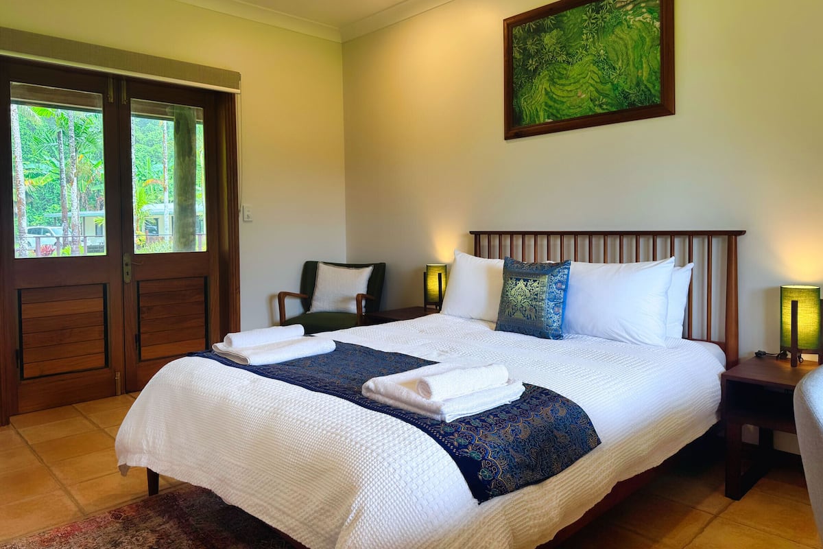 A neatly made bed with white and blue bedding, a green chair, and a painting on the wall.