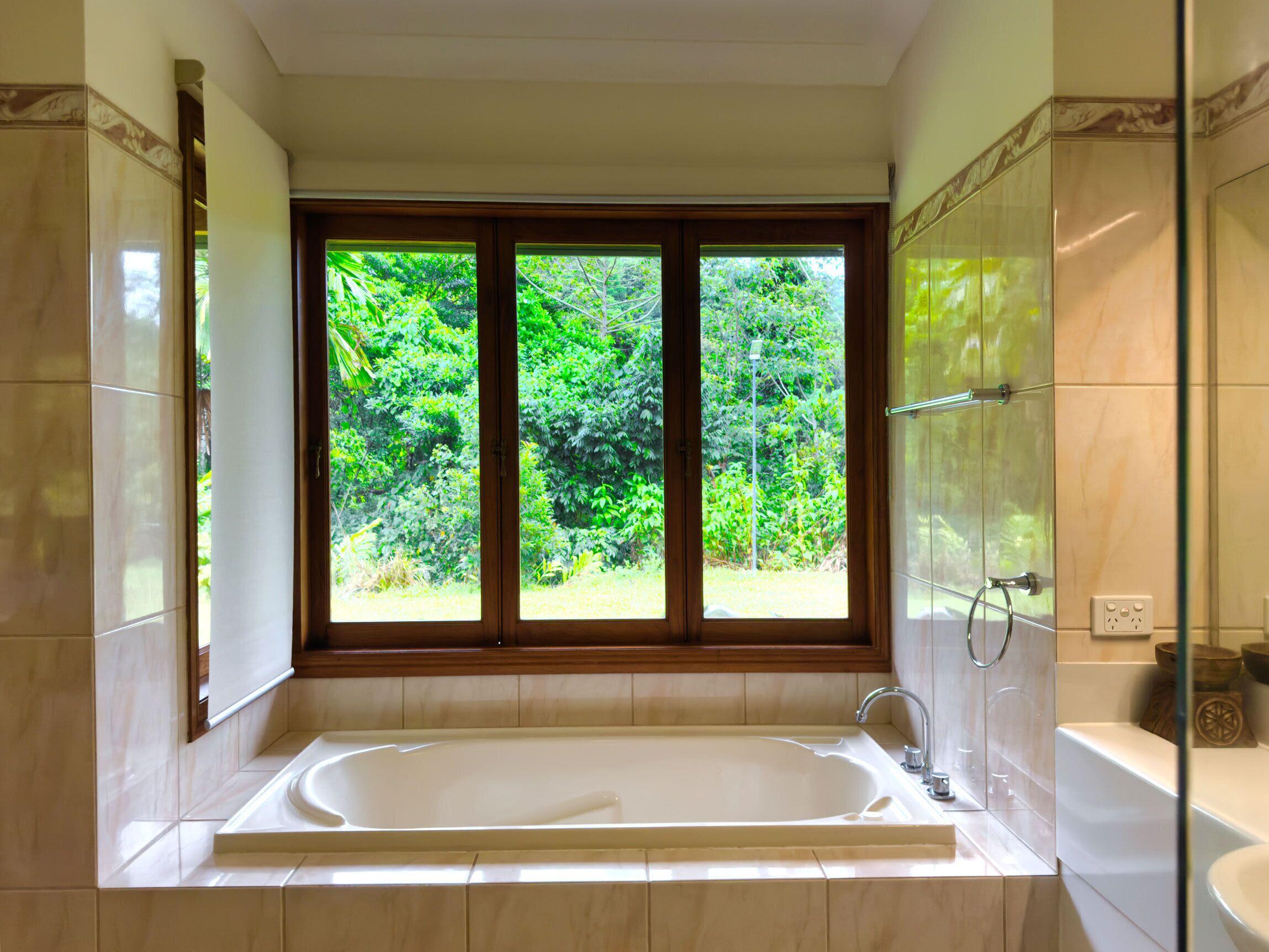 A bathroom with a large bathtub, a shower area, and a window with a view of greenery.